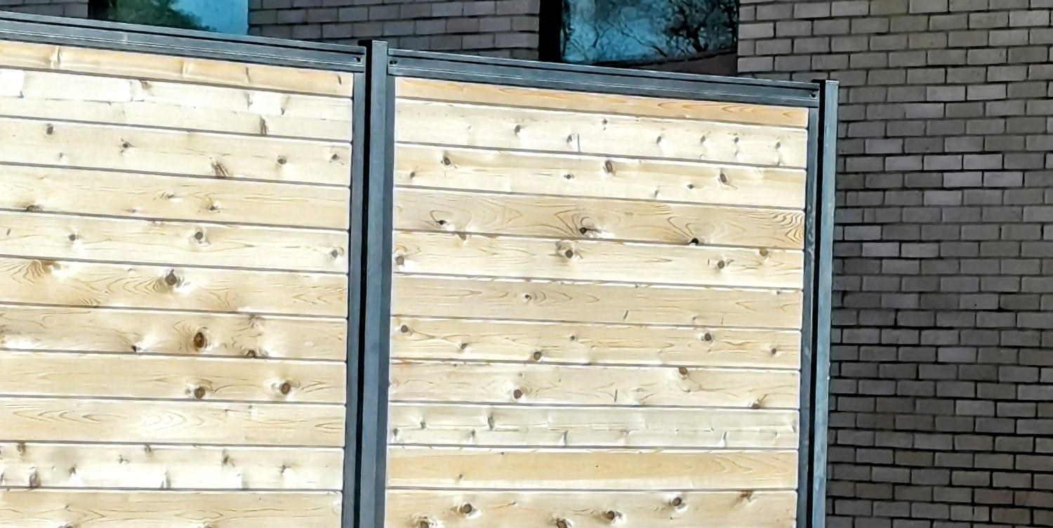 Two horizontal cedar privacy screens set in gray steel frames against a brick medical building.